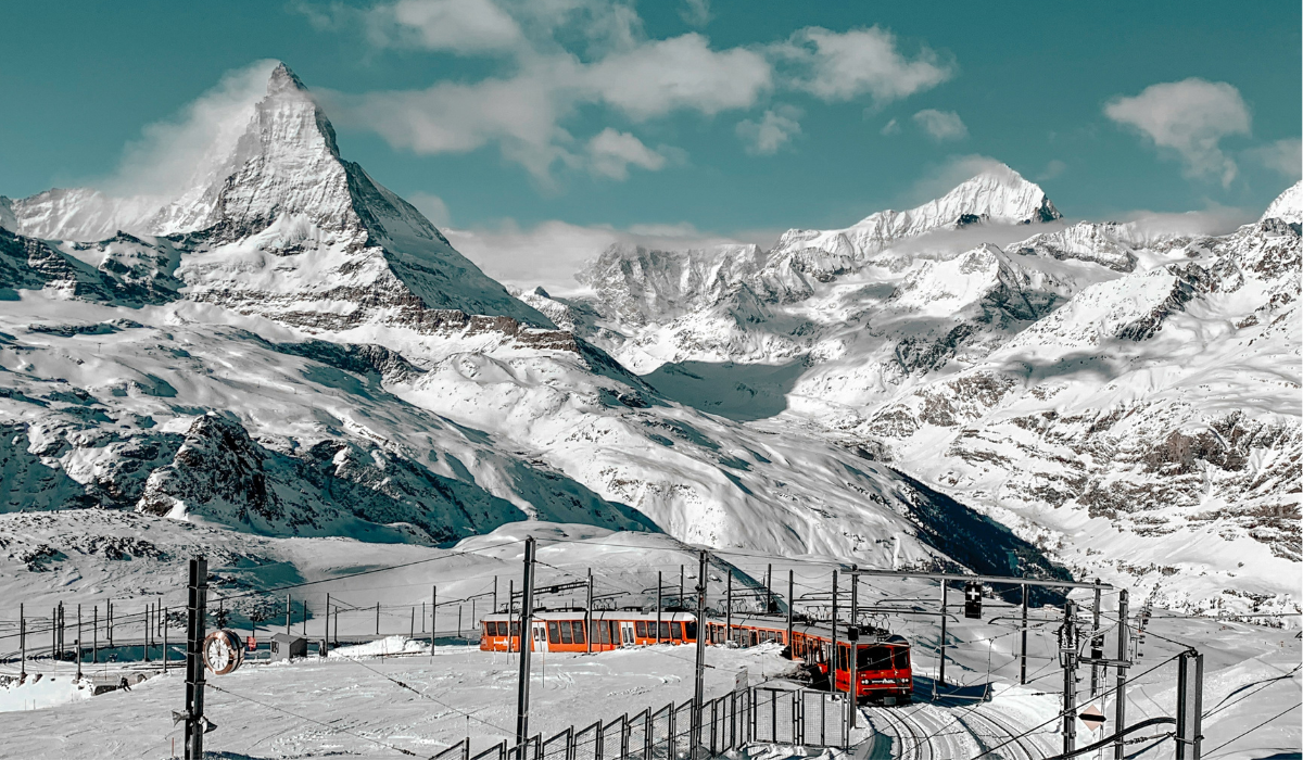 Snowy mountains with the Matterhorn mountain in the background and the red mountain train curving through on the rail line.