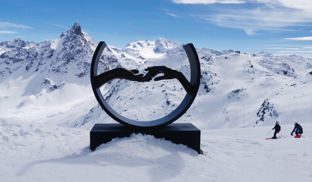 Snowy mountains in the background, with a black scultpure of two hands touching encircled.