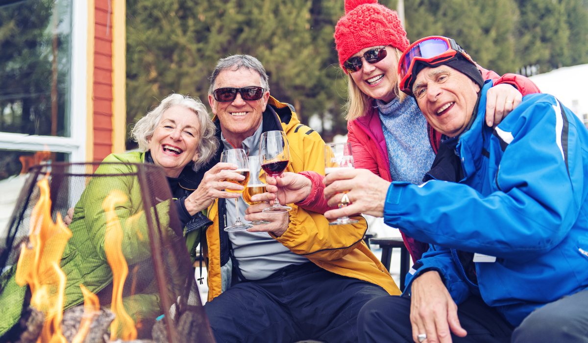 Four middle-aged to elderly people in winter outdoor clothing enjoying a drink and "cheersing".