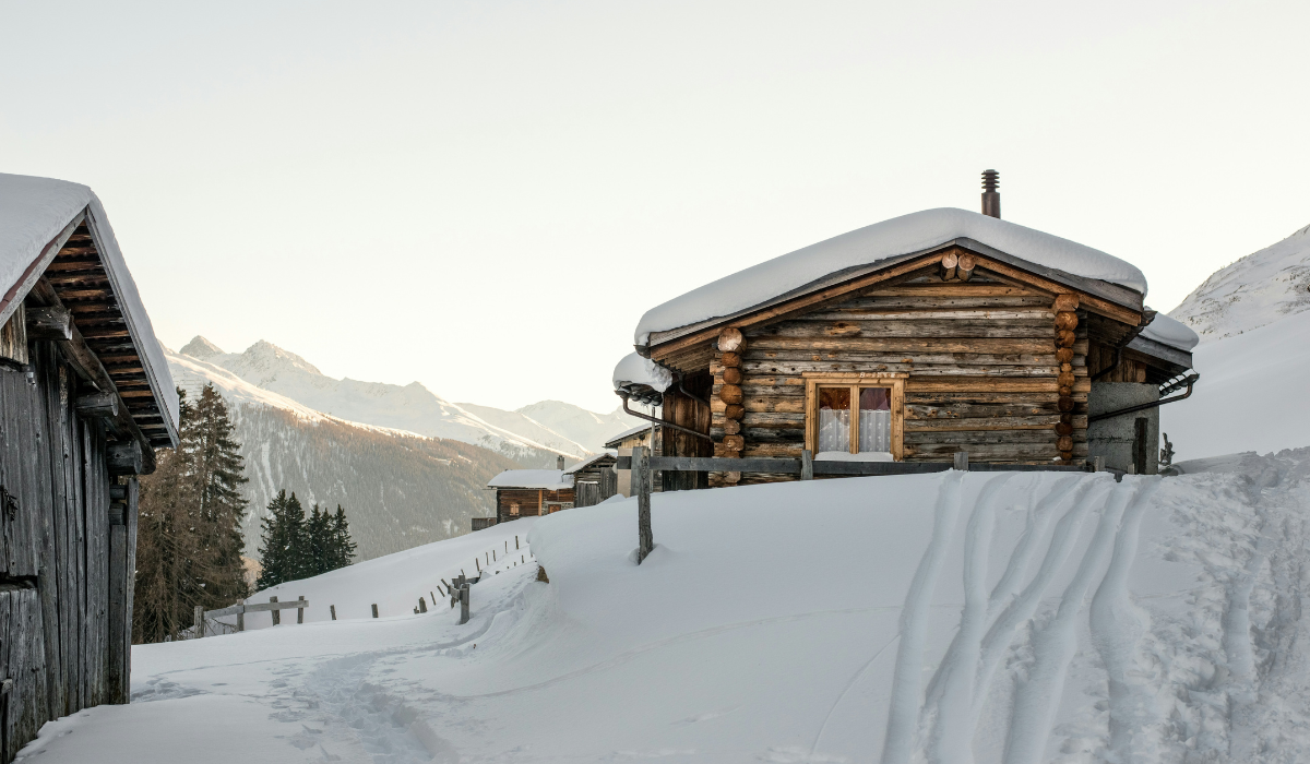 Scenic shot of an oldstyle chalet hut on a snowy hill, mountians in the background.