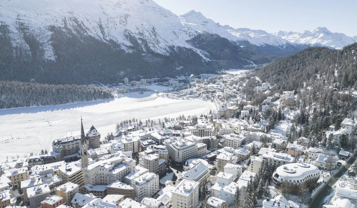 Elevated view St Moritz Lake which is frozen and white, with snowy mountain peaks in the background.