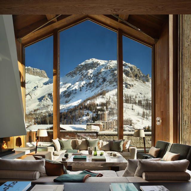 Picture window with snow covered mountain framed in the window, luxury muted interiors with sofa furishings.