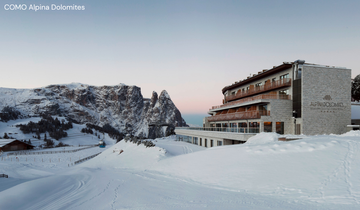 Hotel sitting perched on a platua with mountain peak and snowy slope running past it.