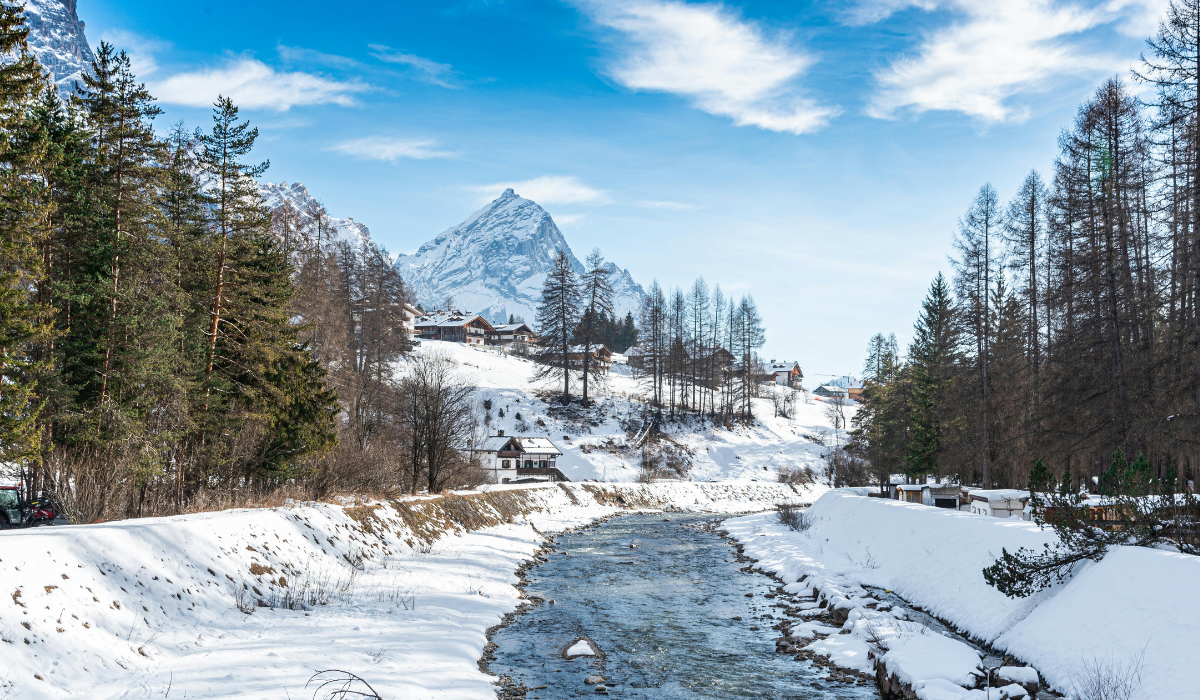Hiking trail over a river with snow on the river bank and a mountain spotted in snow in the background.