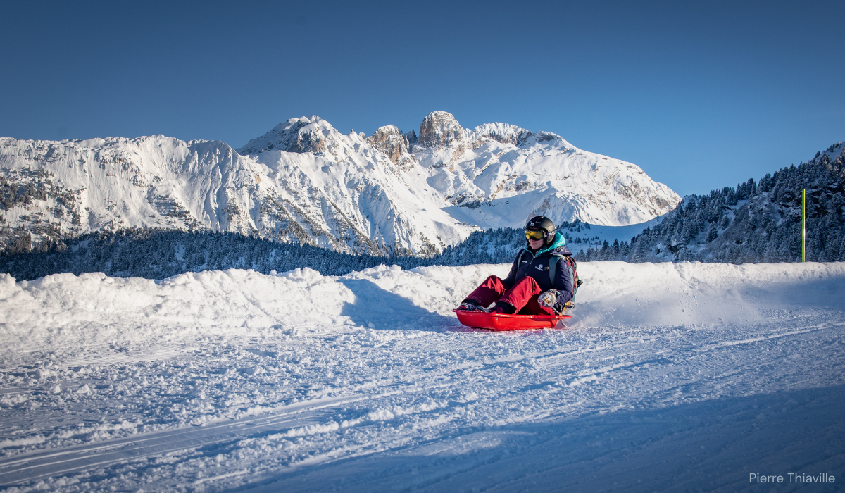 Someone taboggoning down a slight slope, snow and gentle mountains in the background.